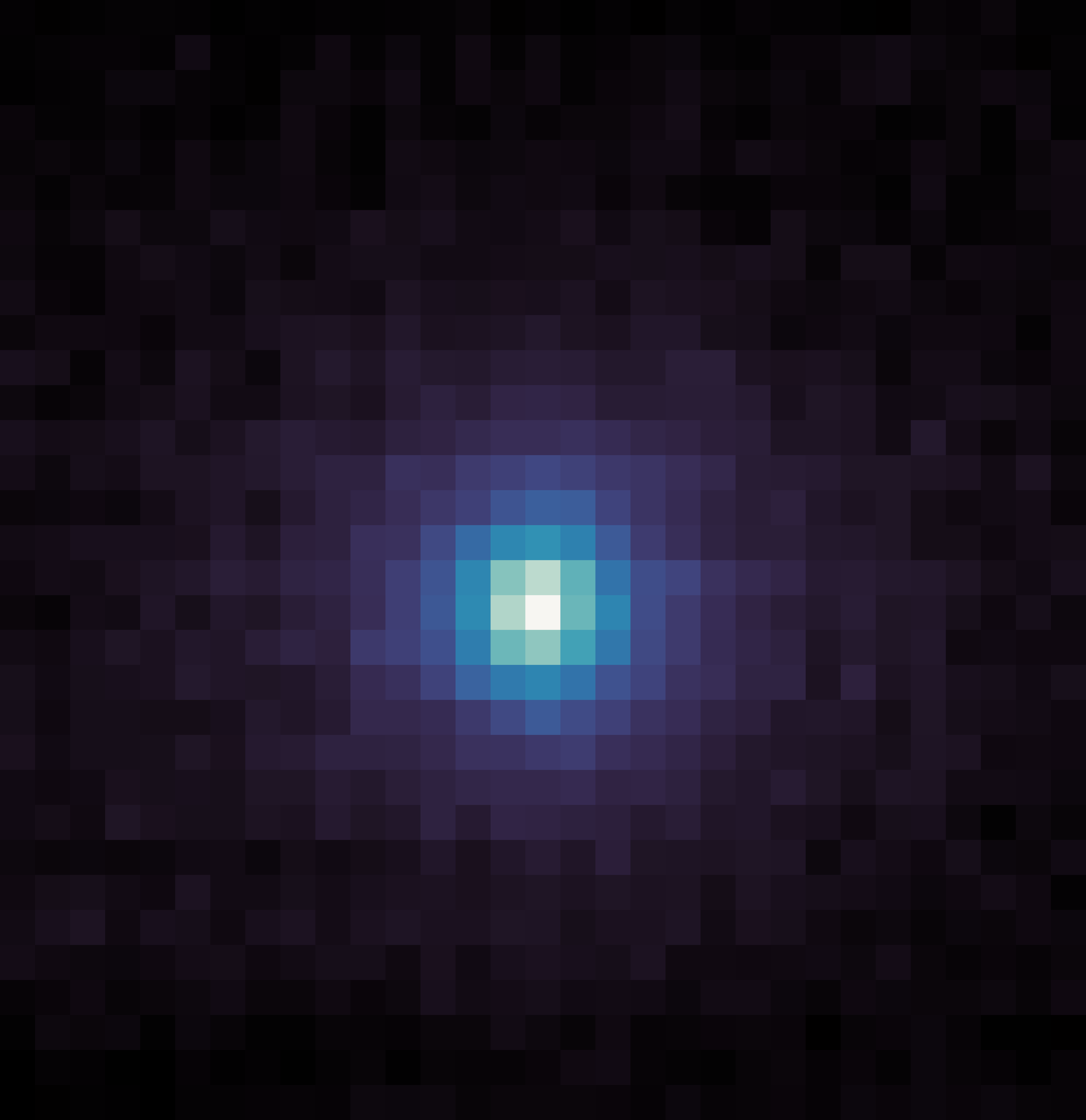 A square, pixelated image with a dark background. At the center is a roughly circular cluster of bright pixels, transitioning from white at the very center to light blue, then darker blue and purple as it spreads outward. The edges and corners of the image are mostly dark purple and black pixels.
